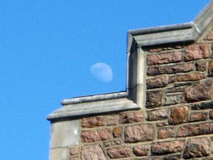 Moon in the afternoon lurking over a building ledge